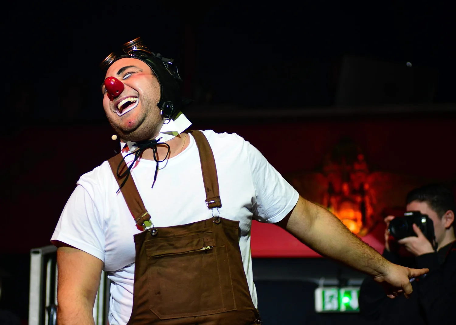 Sacha en clown, bras ouverts sur scène devant le décor de Guignol.